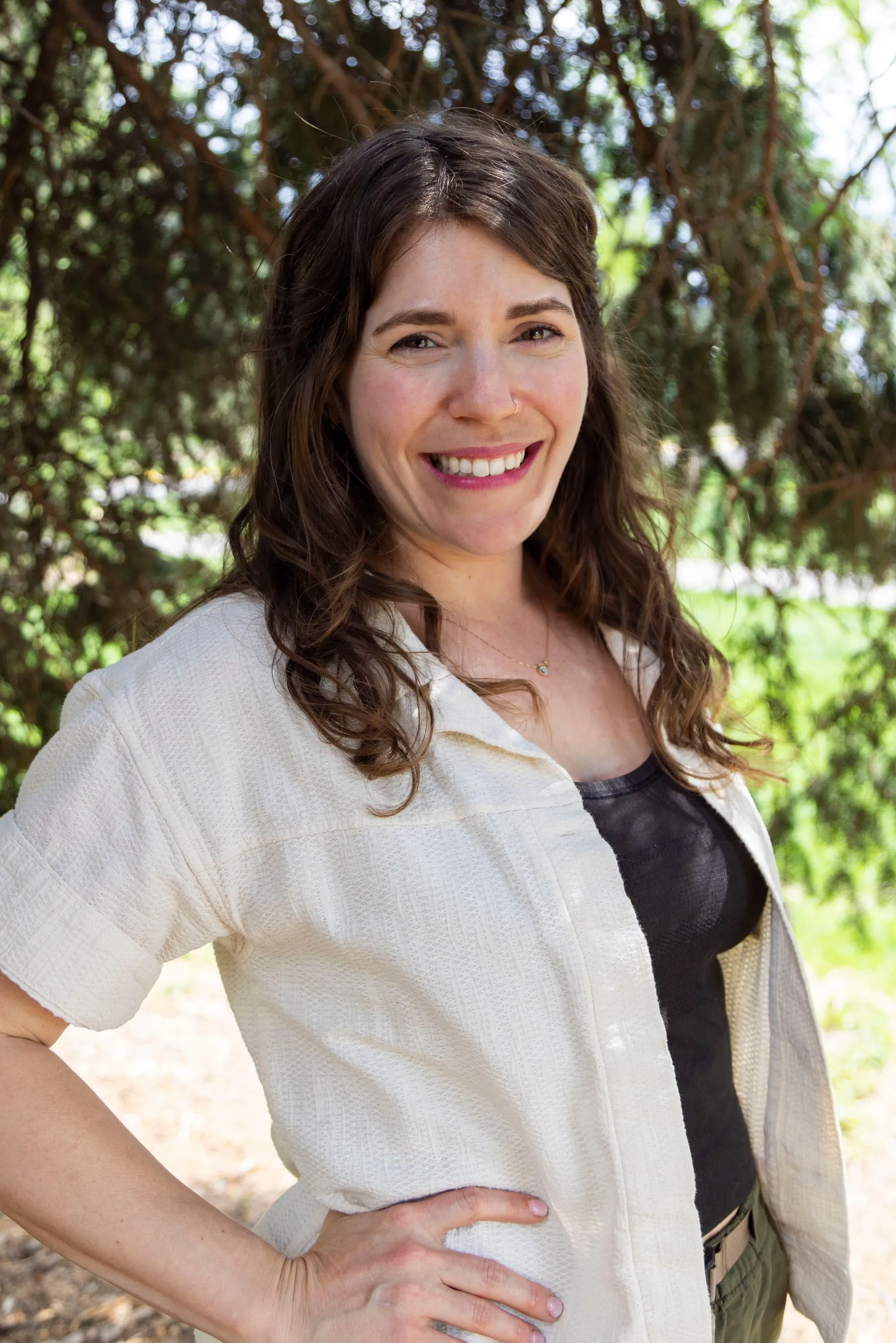 Gina standing outdoors beneath a tree, one hand on her hip, smiling